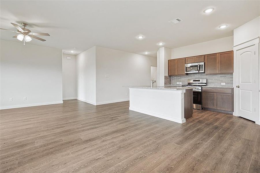 Kitchen with tasteful backsplash, appliances with stainless steel finishes, ceiling fan, dark wood-type flooring, and a kitchen island with sink