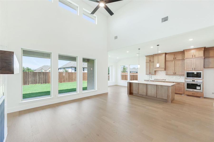 Open-concept living area with two-story ceiling, wood floors, and kitchen with island and stainless appliances