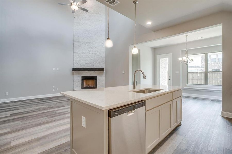 Kitchen featuring light hardwood / wood-style floors, stainless steel dishwasher, ceiling fan with notable chandelier, and an island with sink