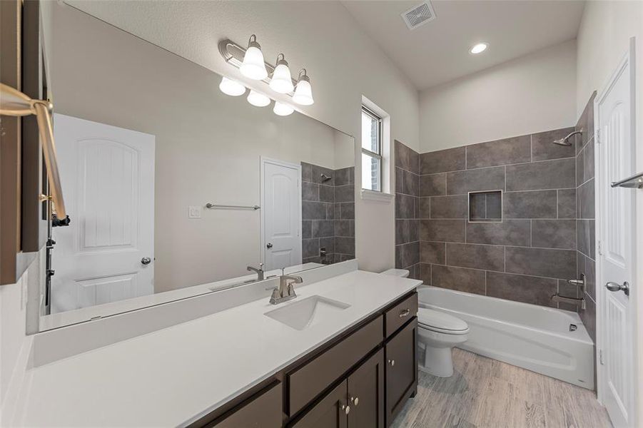 Full bathroom with hardwood / wood-style flooring, vanity, tiled shower / bath combo, and toilet