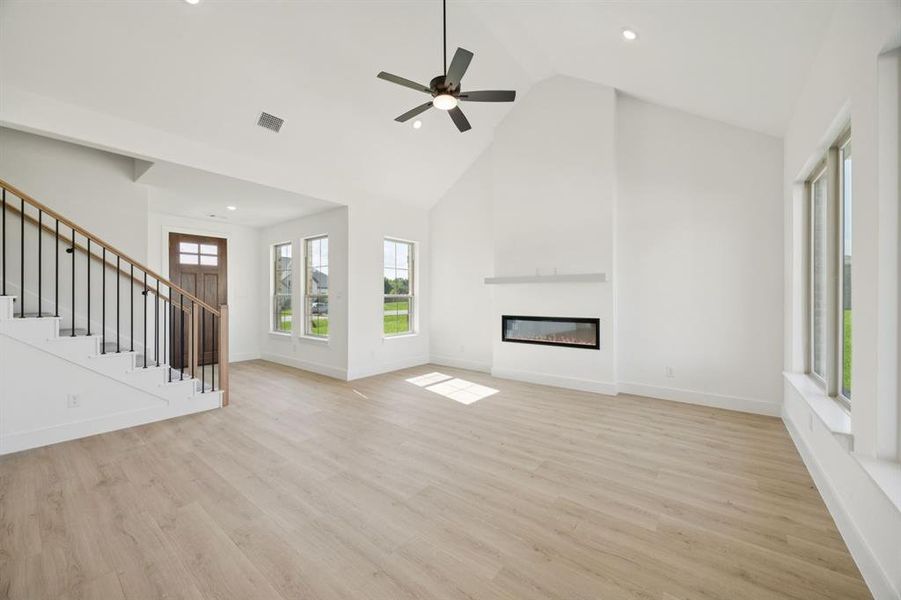 Unfurnished living room featuring high vaulted ceiling, stairs, light wood finished floors, a glass covered fireplace, and recessed lighting Unfurnished living room featuring high vaulted ceiling, stairs, light wood finished floors, a glass covered fireplace, and recessed lighting