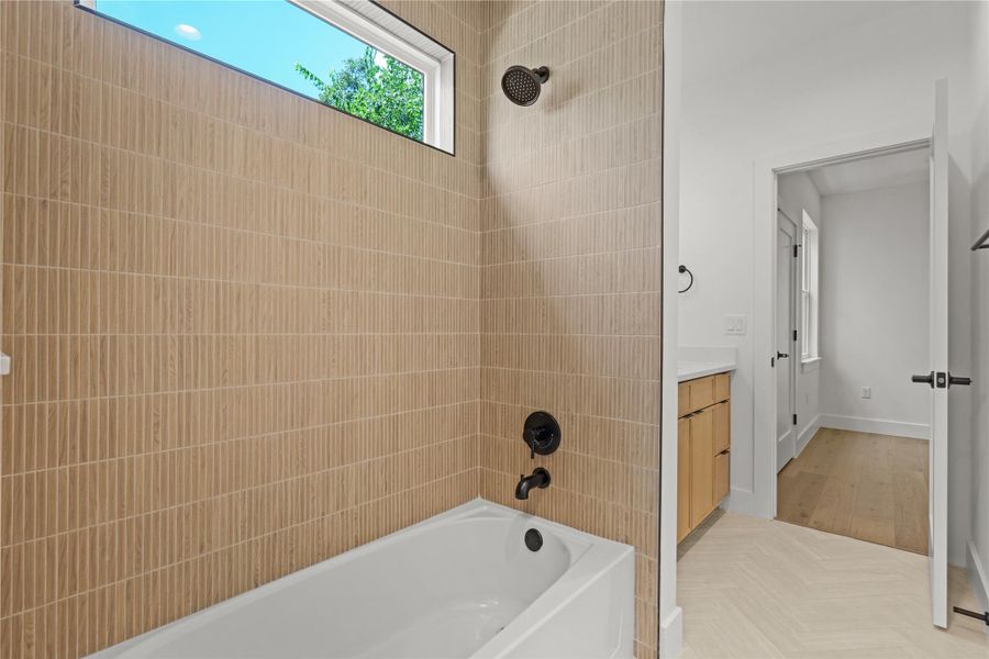 A well-lit primary bath features a spacious soaking tub with a rain showerhead and light wood-patterned tile.