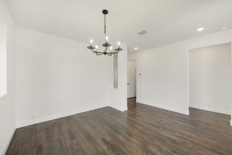Empty dining room with dark hardwood floors, white walls, and black chandelier overhead.