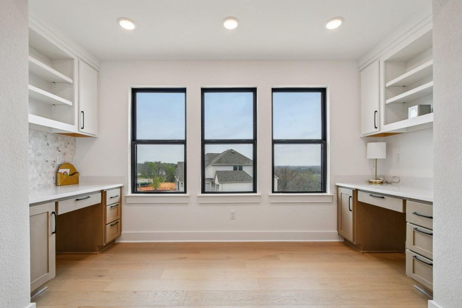 The property features a bright room with three windows, built-in desks, shelving, and light wood flooring The property features a bright room with three windows, built-in desks, shelving, and light wood flooring