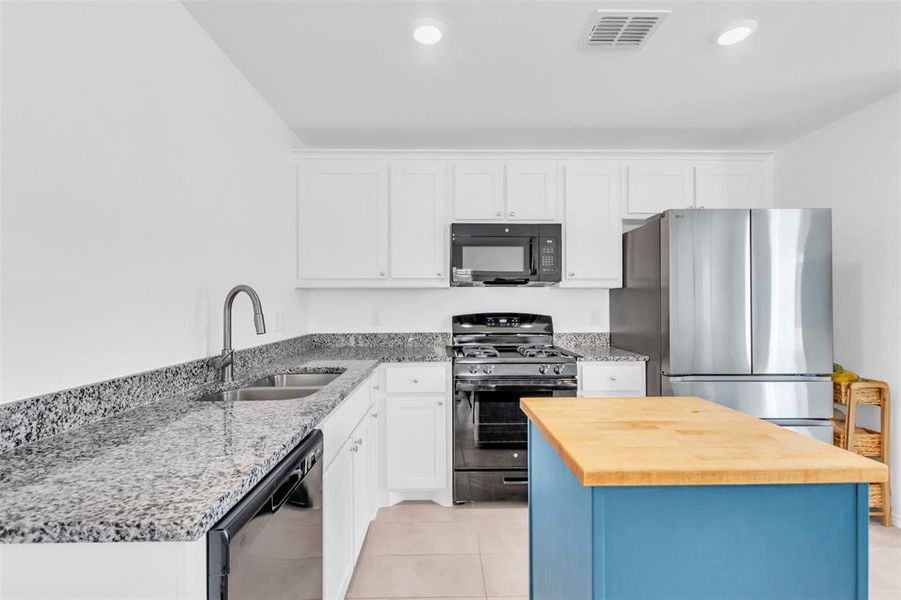 Kitchen with black appliances, butcher block countertops, white cabinetry, blue cabinetry, and light tile patterned floors