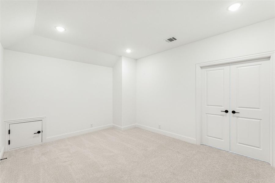 Empty room with white walls, carpet flooring, double closet doors, and a small access panel near the floor