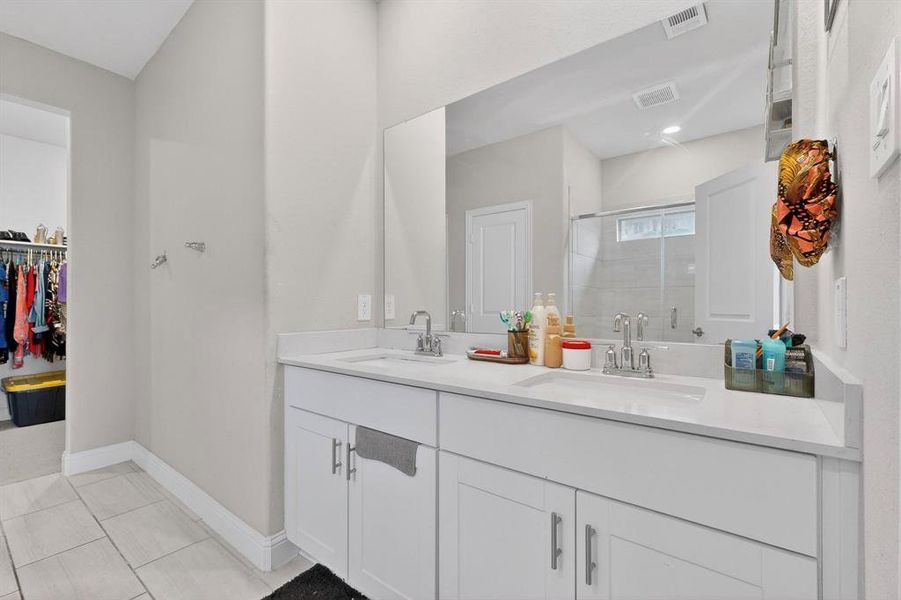 Bathroom featuring double vanity, a walk in closet, a stall shower, and light tile patterned floors Bathroom featuring double vanity, a walk in closet, a stall shower, and light tile patterned floors
