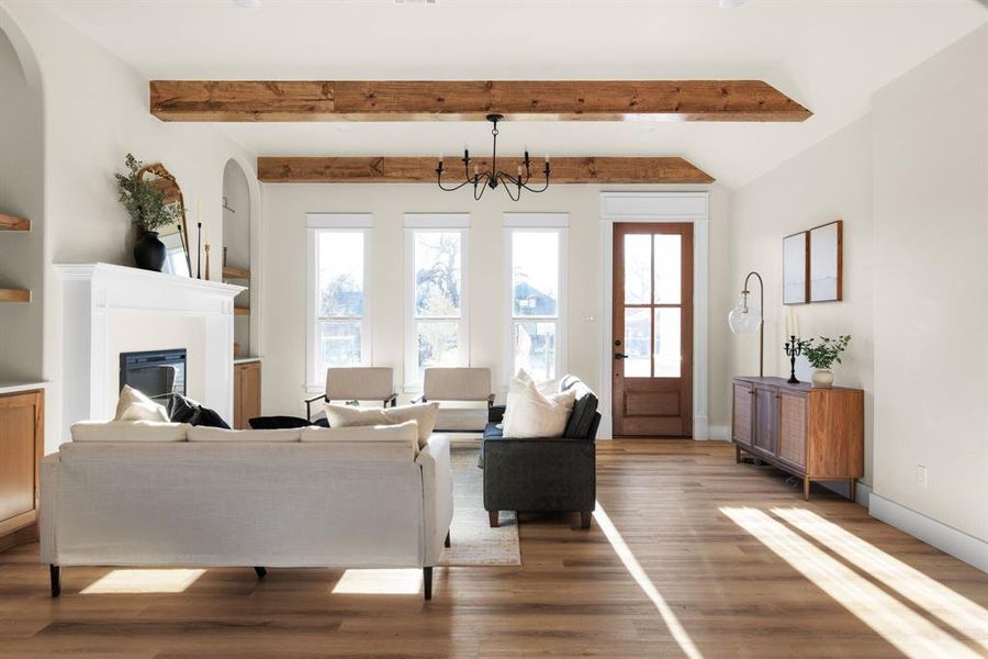 Living room featuring beamed ceiling, wood-type flooring, and a notable chandelier