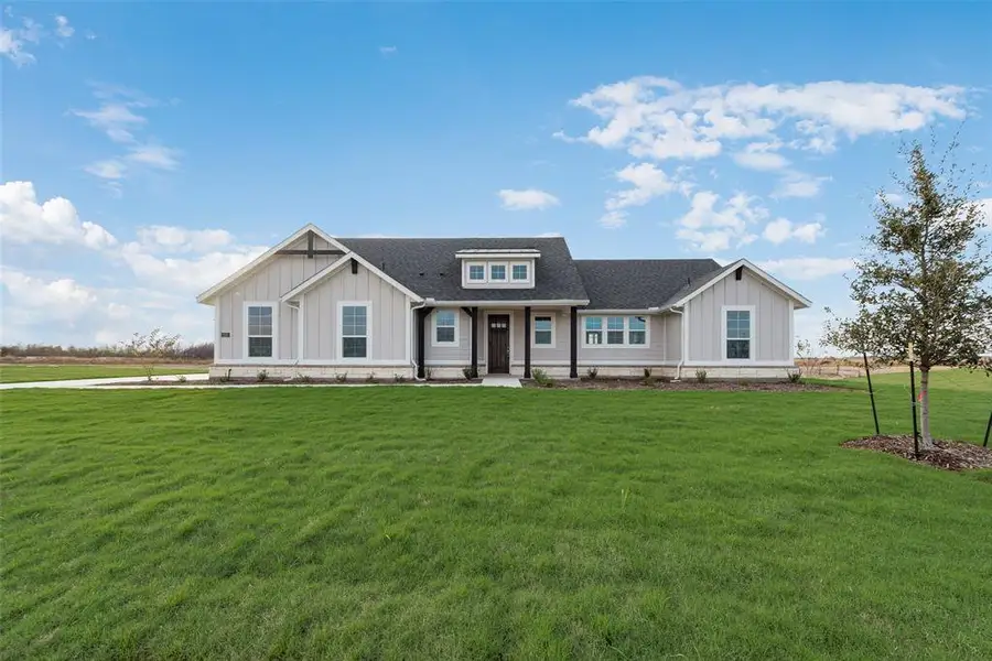 Modern farmhouse with a shingled roof, board and batten siding, covered porch, and a front lawn