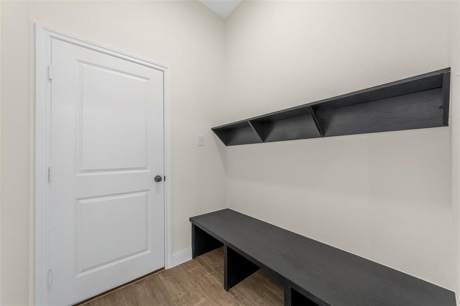 Entryway featuring wood-finish flooring, a white panel door, and a built-in dark wood bench with coordinating overhead shelving