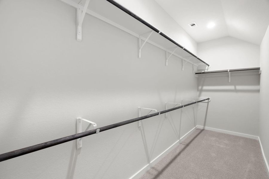spacious walk-in closet with high ceilings and plush carpet. Warm paint tones, built-in shelving, and dark finishes create a contemporary and functional retreat. Sample photo of completed home with similar floor plan. Actual colors and selections may vary. spacious walk-in closet with high ceilings and plush carpet. Warm paint tones, built-in shelving, and dark finishes create a contemporary and functional retreat. Sample photo of completed home with similar floor plan. Actual colors and selections may vary.