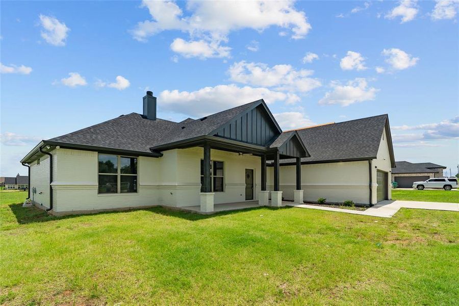 Rear view of property with a shingled roof, driveway, a yard, a garage, and board and batten siding Rear view of property with a shingled roof, driveway, a yard, a garage, and board and batten siding