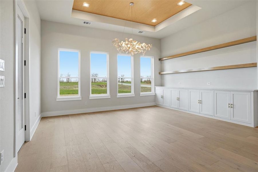 Elegant dining area featuring a tray ceiling with wood detail, designer chandelier, built-in cabinetry, and floating shelves.