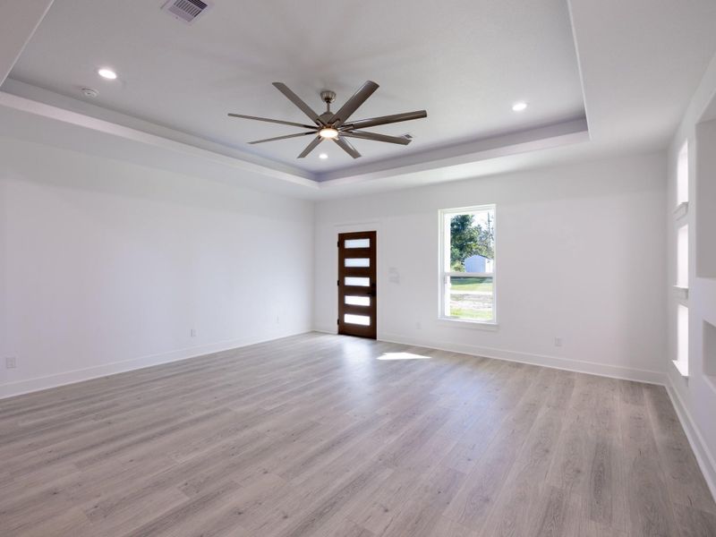 Bright, spacious room featuring modern wood flooring, a stylish ceiling fan, and a sleek door with horizontal glass panels. The large window allows plenty of natural light, enhancing the room's airy feel.