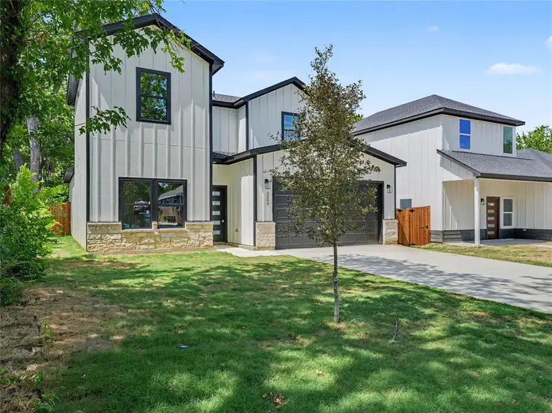 Modern farmhouse-style exterior featuring vertical board and batten siding, black-framed windows, stone accents, a two-car garage, and a concrete driveway Modern farmhouse-style exterior featuring vertical board and batten siding, black-framed windows, stone accents, a two-car garage, and a concrete driveway