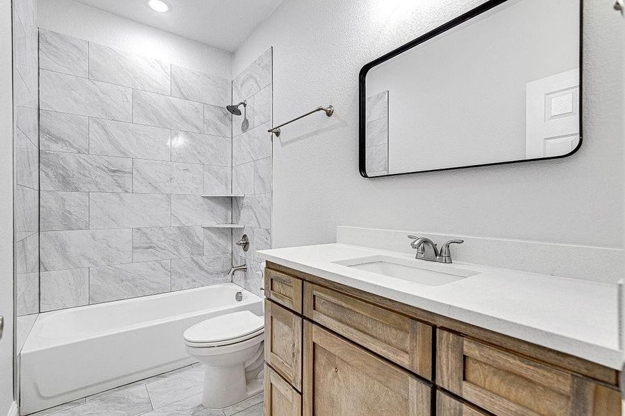 Full bathroom featuring toilet, tile patterned floors, tiled shower / bath combo, and vanity