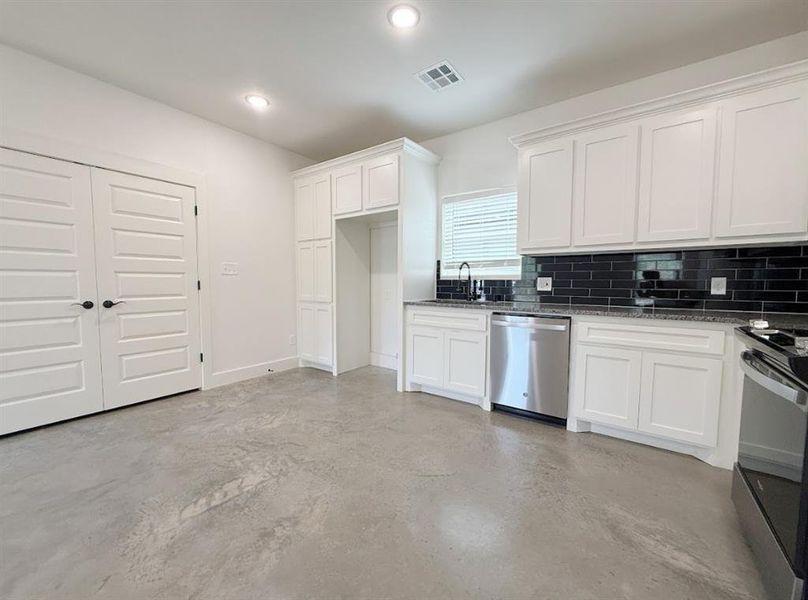 Kitchen featuring white cabinetry, tasteful backsplash, dark stone counters, finished concrete flooring, and recessed lighting Kitchen featuring white cabinetry, tasteful backsplash, dark stone counters, finished concrete flooring, and recessed lighting