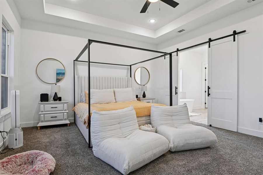 Carpeted bedroom with a tray ceiling, a barn door, ceiling fan, recessed lighting, and ensuite bathroom Carpeted bedroom with a tray ceiling, a barn door, ceiling fan, recessed lighting, and ensuite bathroom