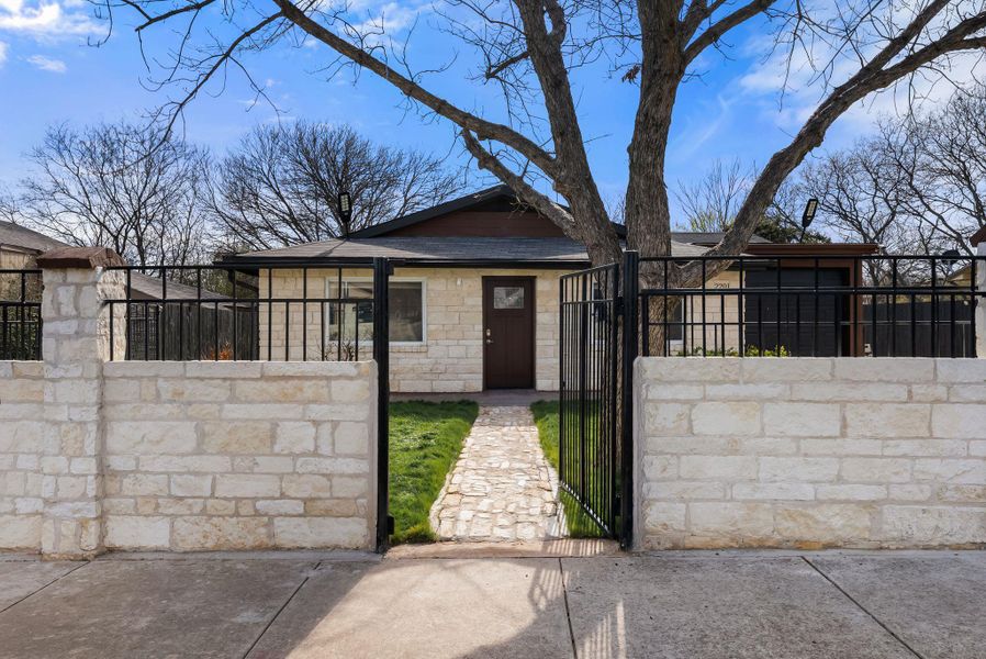 View of front of house with a gate, a fenced front yard, stone siding, and roof with shingles