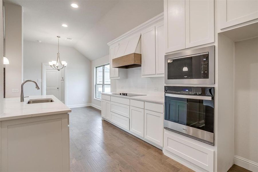 Kitchen featuring light stone countertops, stainless steel appliances, light hardwood / wood-style floors, a notable chandelier, and sink