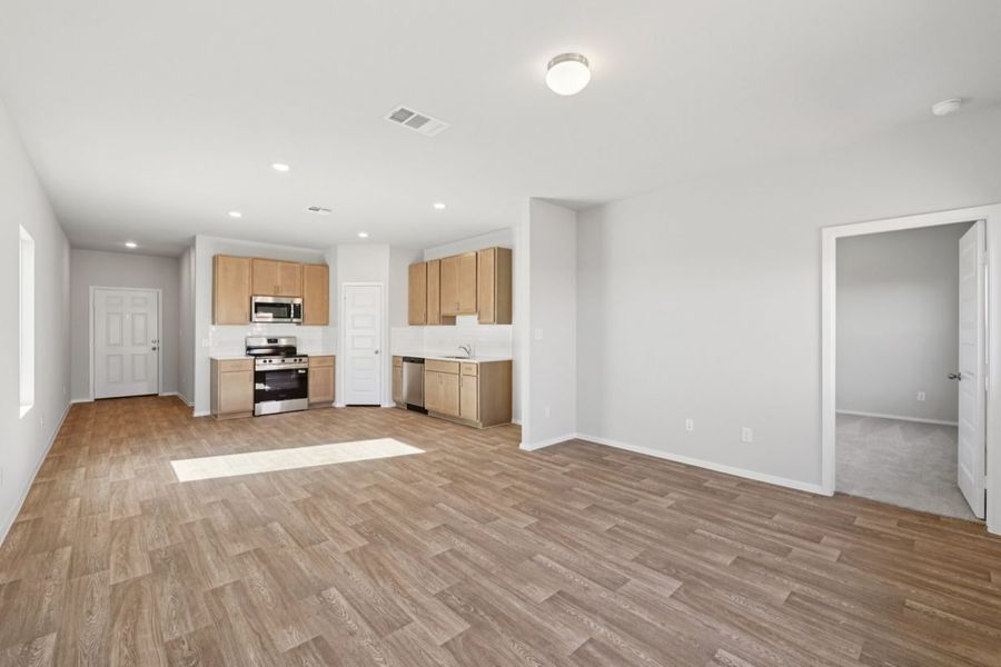 Image of a living room with light grey walls, wood-look vinyl flooring, and an open kitchen in the distance