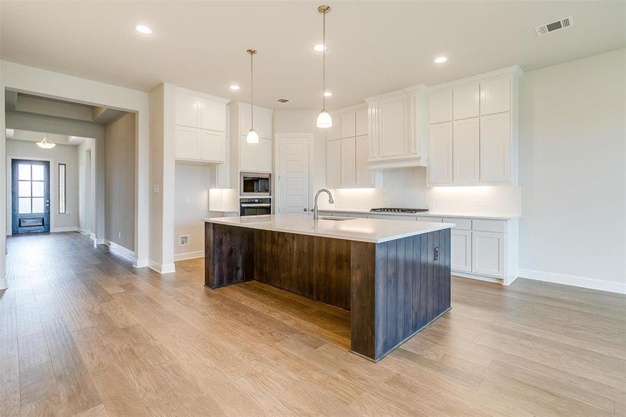 Kitchen with white cabinetry, light hardwood / wood-style floors, appliances with stainless steel finishes, and an island with sink