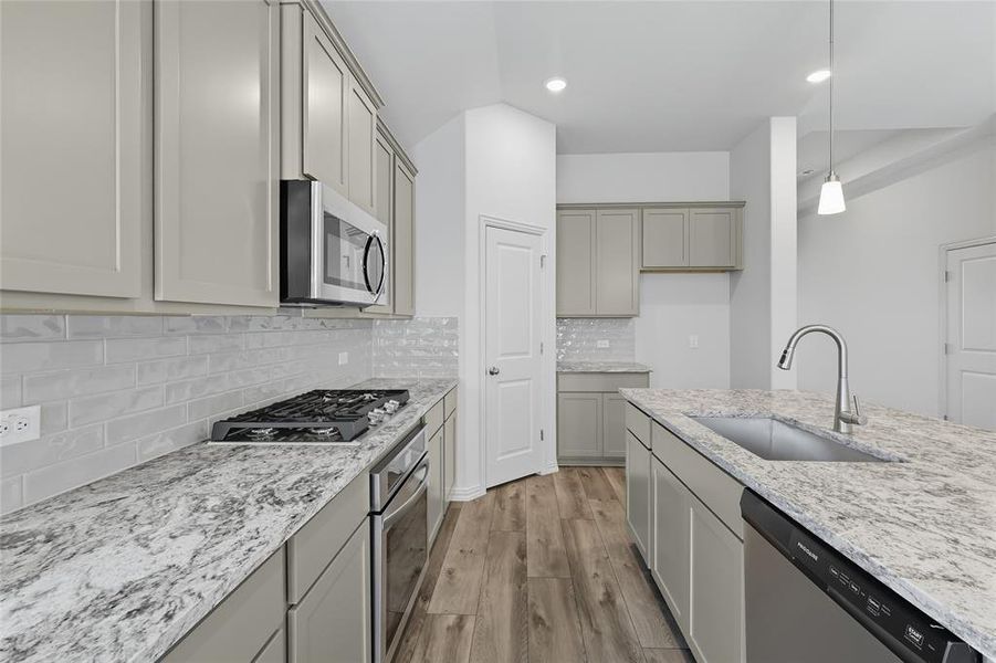 Kitchen with hanging light fixtures, stainless steel appliances, light wood finished floors, light stone counters, and gray cabinets Kitchen with hanging light fixtures, stainless steel appliances, light wood finished floors, light stone counters, and gray cabinets