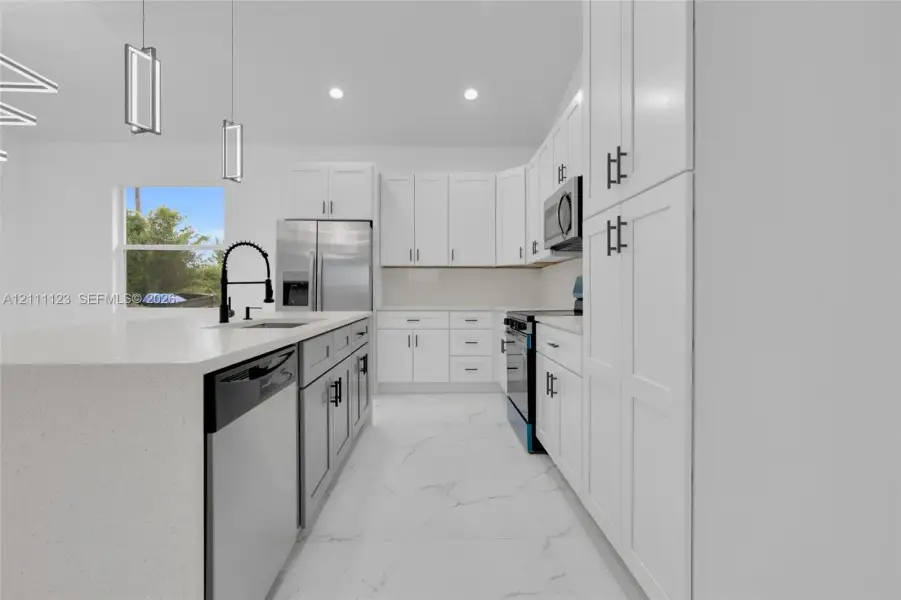 Island with sink, black faucet, and stainless steel dishwasher alongside off-white cabinetry.