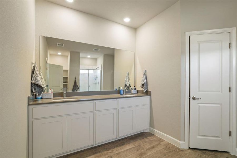 Full bath featuring a shower stall, double vanity, light wood-type flooring, and a walk in closet Full bath featuring a shower stall, double vanity, light wood-type flooring, and a walk in closet