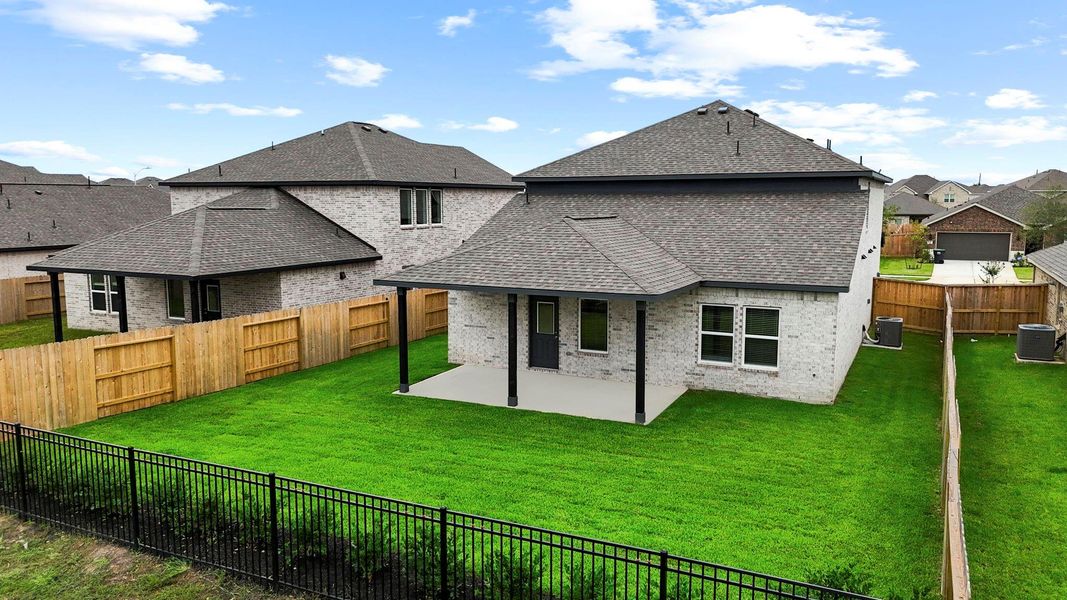 Rear view of the home reveals the full brick exterior and extended patio area with covered space—backing to wrought iron fencing and offering scenic views with no immediate rear neighbors.