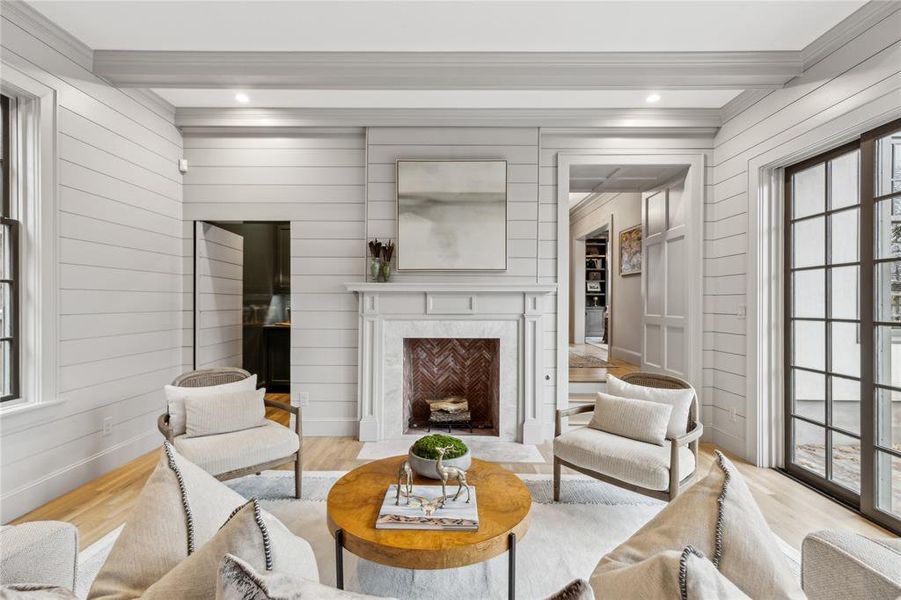 Living area with baseboards, a premium fireplace, beamed ceiling, crown molding, and light wood-type flooring