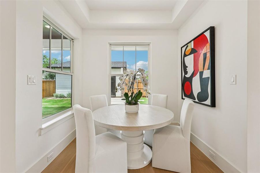 Bright dining area featuring wood-finish flooring, white walls, and a tray ceiling