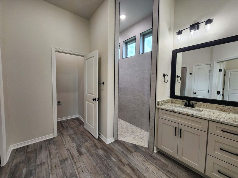 Bathroom featuring wood-finish flooring, a double vanity with granite countertop, undermount sinks, and a large frameless mirror