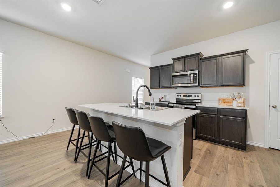Kitchen with a kitchen breakfast bar, appliances with stainless steel finishes, light LVP floors, an island with sink, and recessed lighting Kitchen with a kitchen breakfast bar, appliances with stainless steel finishes, light LVP floors, an island with sink, and recessed lighting