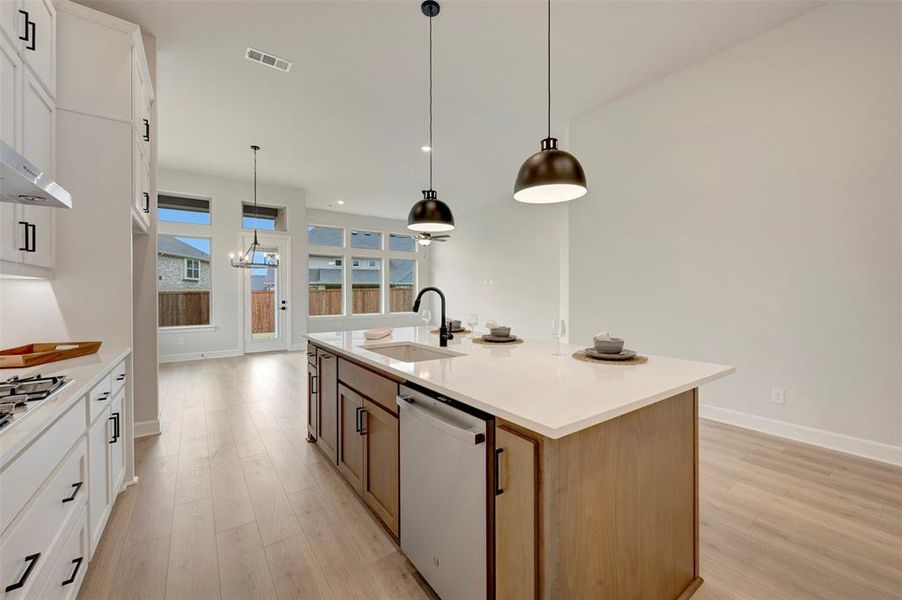 Kitchen with two tone color scheme, dishwasher, light wood finished floors, pendant lighting, and an island with sink