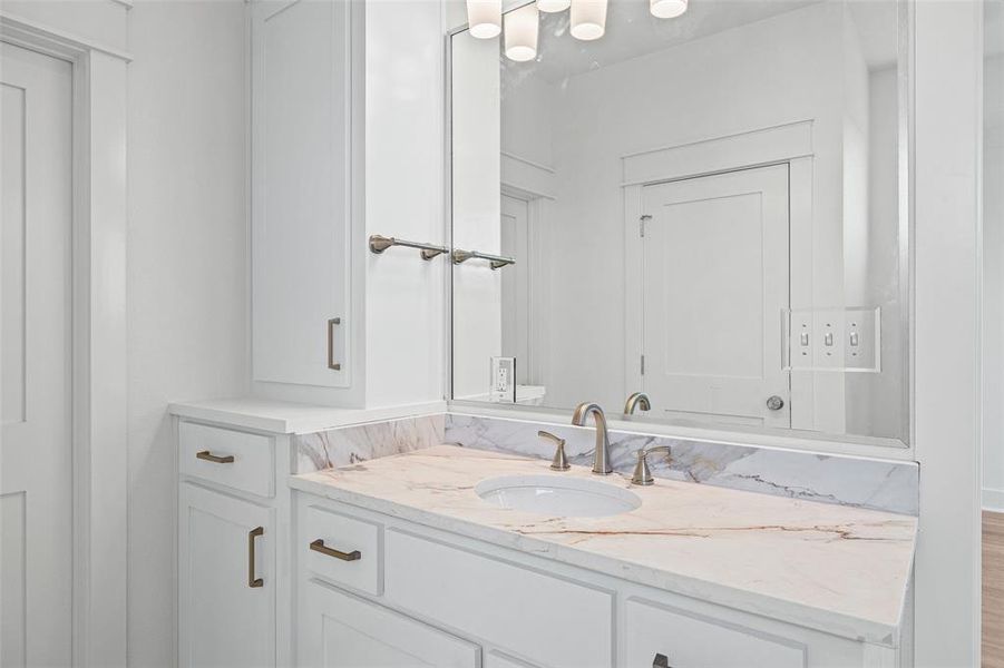 Vanity featuring white cabinetry with brushed bronze hardware, an undermount sink, and a stone countertop with veining