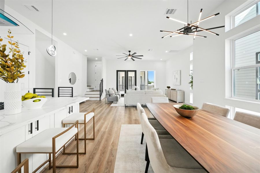 Spacious open-concept living and dining area with modern design and abundant natural light, featuring high ceilings, wide-plank wood flooring, and designer lighting fixtures. The seamless layout connects the dining space, kitchen with Quartz countertops and breakfast bar seating, and the bright living area with large windows and balcony access Spacious open-concept living and dining area with modern design and abundant natural light, featuring high ceilings, wide-plank wood flooring, and designer lighting fixtures. The seamless layout connects the dining space, kitchen with Quartz countertops and breakfast bar seating, and the bright living area with large windows and balcony access