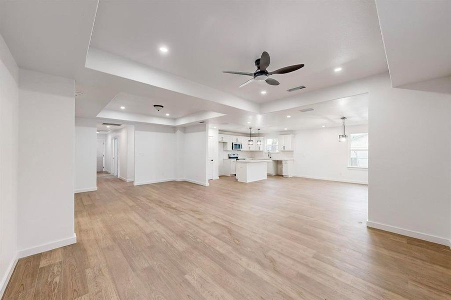 Unfurnished living room with a tray ceiling, ceiling fan, and light hardwood / wood-style flooring