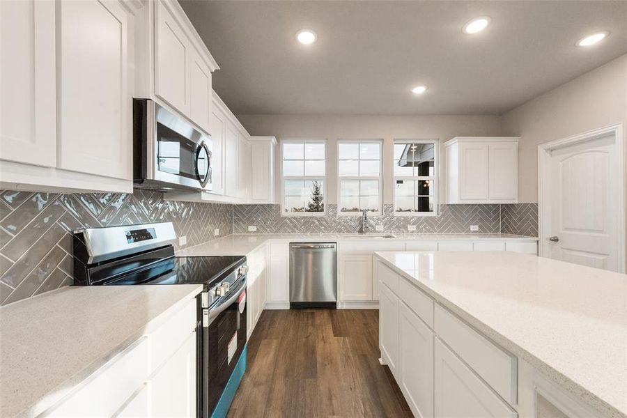 Kitchen featuring stainless steel appliances, white cabinetry, light stone countertops, dark wood-type flooring, and recessed lighting