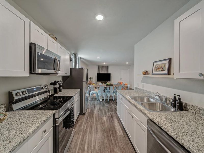 Kitchen with stainless steel appliances, white cabinetry, dark wood-type flooring, open floor plan, and light stone countertops