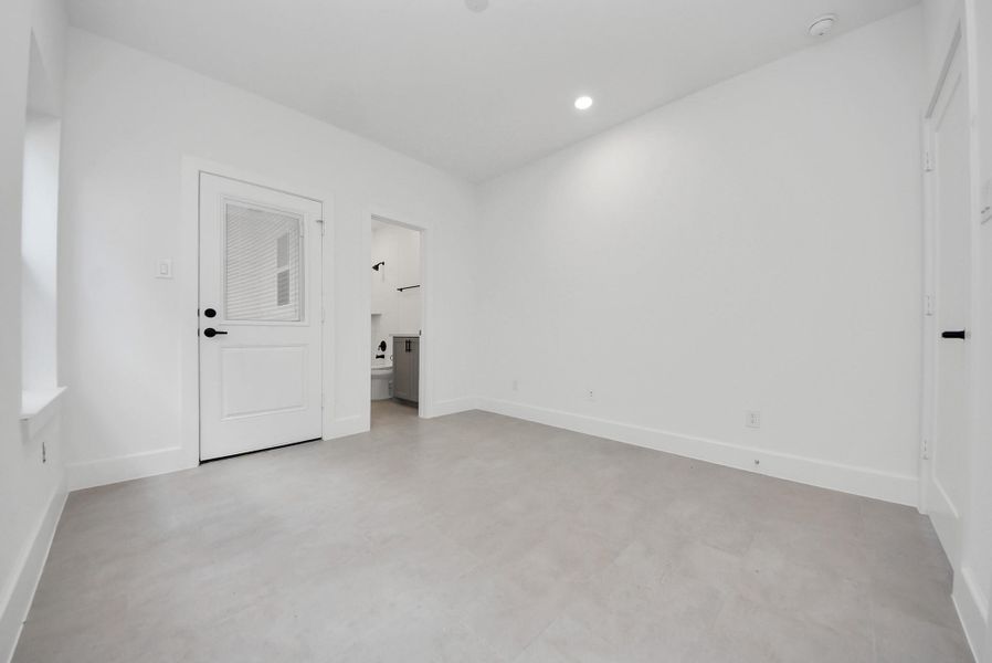 Here is a bright, minimalist utility or mudroom area, with neutral-toned flooring and white walls. Convenient access to the outdoors and an adjacent bath or laundry area makes it both stylish and functional.