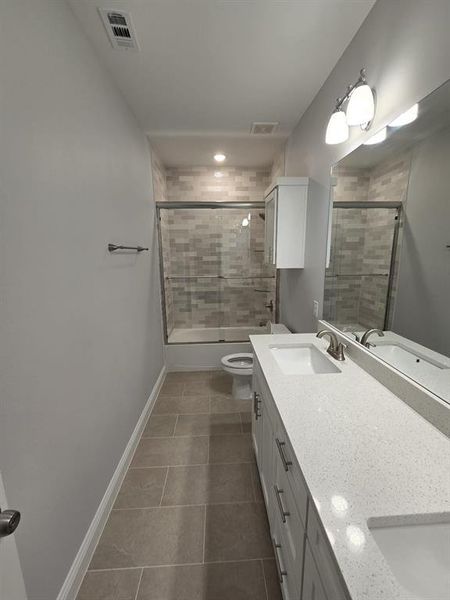 Full bathroom with tile patterned floors, bath / shower combo with glass door, dual vanity, and toilet