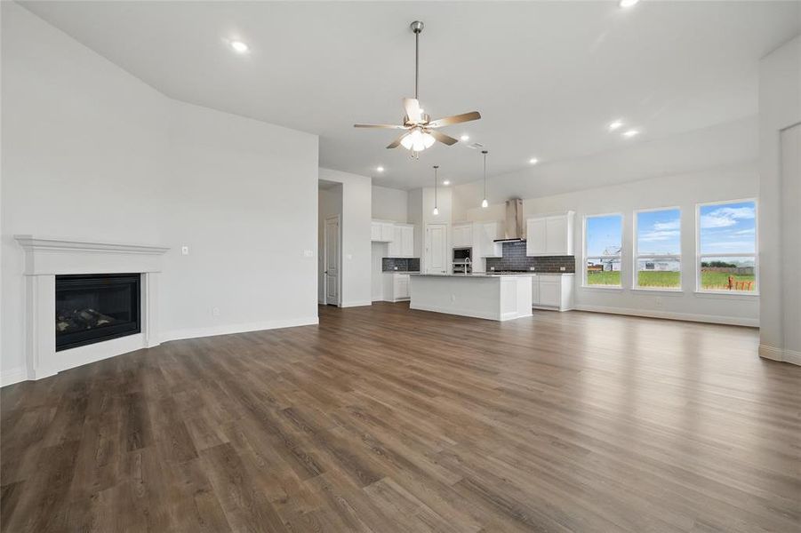 Unfurnished living room with a glass covered fireplace, baseboards, ceiling fan, recessed lighting, and dark wood finished floors