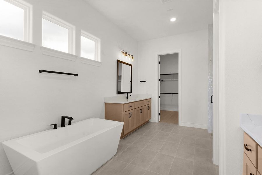 Indulge in this serene primary bathroom featuring a freestanding tub, dual vanities, and a convenient walk-in closet.