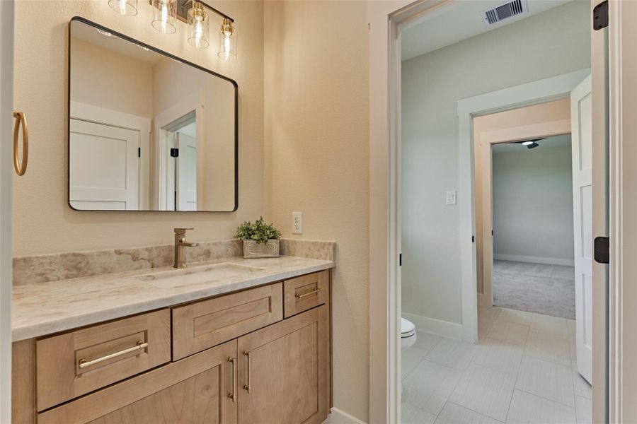 The bedroom 4 side of the Jack-and-Jill bath — a private vanity with natural wood cabinetry, warm gold fixtures, and a large framed mirror, with a shared central toilet and tub. Each bedroom enjoys its own dedicated sink and vanity space. The bedroom 4 side of the Jack-and-Jill bath — a private vanity with natural wood cabinetry, warm gold fixtures, and a large framed mirror, with a shared central toilet and tub. Each bedroom enjoys its own dedicated sink and vanity space.