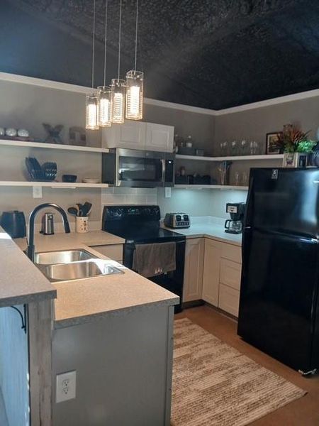 Kitchen featuring black appliances, open shelves, light countertops, hanging light fixtures, and a kitchen bar