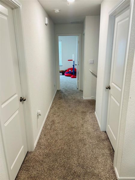Carpeted hallway featuring bright white walls, white trim, and white doors with dark hardware Carpeted hallway featuring bright white walls, white trim, and white doors with dark hardware