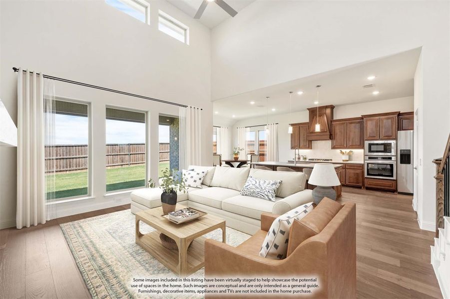 Open-concept living room with two-story ceiling, hardwood floors, and kitchen visible in background Open-concept living room with two-story ceiling, hardwood floors, and kitchen visible in background