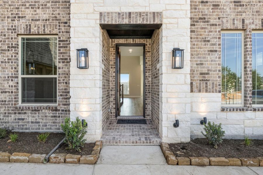 Front entry of brick home with stone-framed doorway, black door, and two wall lanterns flanking the entrance Front entry of brick home with stone-framed doorway, black door, and two wall lanterns flanking the entrance