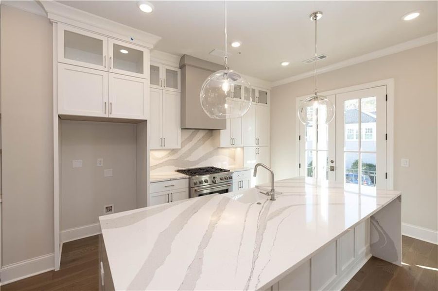 Kitchen with glass insert cabinets, white cabinets, light stone counters, backsplash, and hanging light fixtures